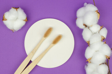 Two wooden toothbrushes and cotton flowers on a purple background. Personal hygiene items