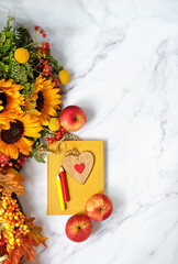 autumn seasonal composition with decorative heart, pencils, book, autumn flowers bouquet, apples close up on abstract marble background. fall time concept. flat lay. copy space