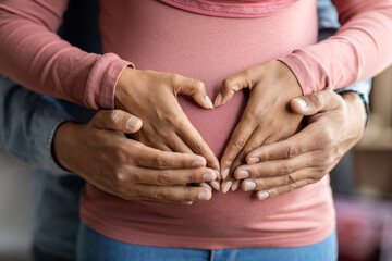 Black muslim couple making heart shape on pregnant belly with their hands