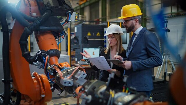 Chief engineer and project manager in modern industrial factory with robot arms talking and planning optimization of production.