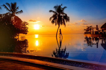 Sunset on Maldives island, luxury water villas resort, pool and palm tree. Beautiful sky and beach...