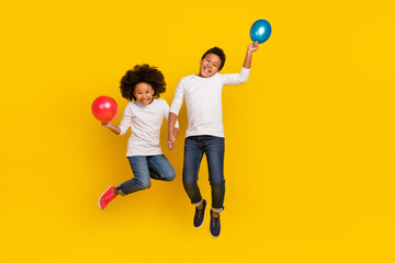 Full size photo of two excited energetic pupils hold hands air balloon isolated on yellow color background © deagreez