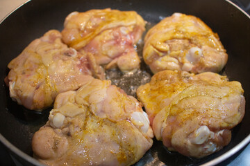 Roasted chicken thighs on a frying black non-stick pan. Fresh fried chicken with curry, tumeric and coriander.