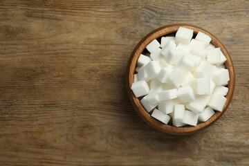 Fototapeta na wymiar Bowl of white sugar cubes on wooden table, top view. Space for text