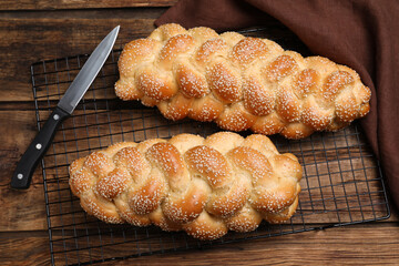 Homemade braided breads with knife, napkin and cooling rack on wooden table, flat lay. Traditional Shabbat challah