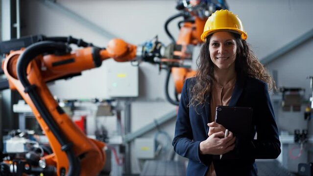 Automation female engineer with tablet for programming robotic arm in factory.
