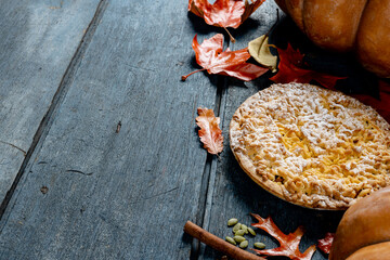 Composition of autumn leaves, pumpkins, spices and pie on wooden background