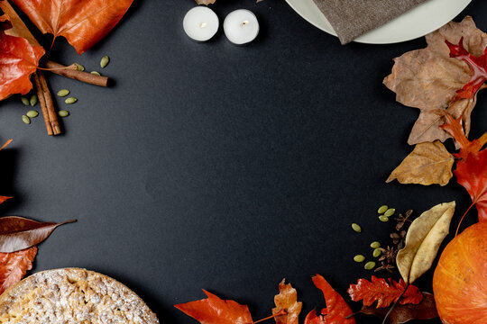 Composition of autumn leaves, pumpkins, spices and pie on black background