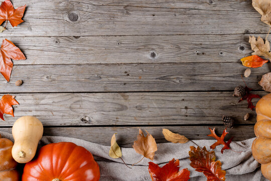 Composition of pumpkins with pinecones and autumn leaves on wooden background
