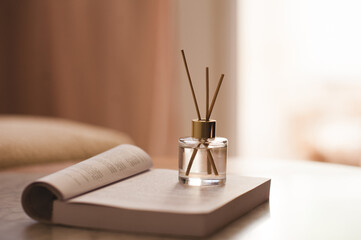 Home liquid scented fragrance in glass bottle with bamboo sticks on open folded paper book on table in bedroom close up. Cozy atmosphere.