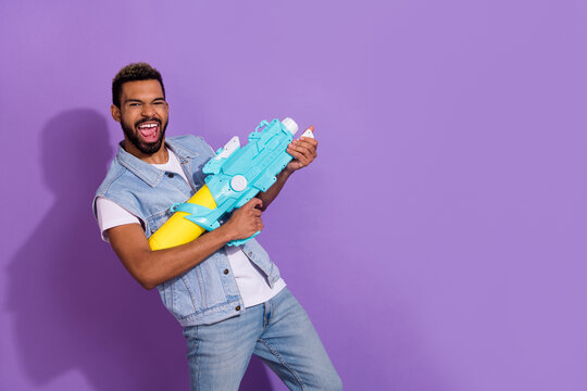 Photo of charming cool man wear jeans waistcoat showing water gun empty space isolated violet color background