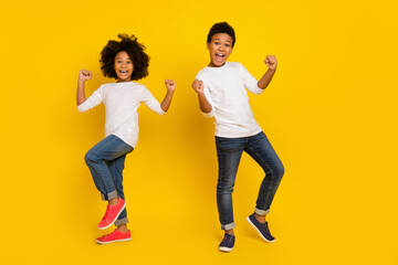 Photo of funky lucky schoolboy schoolgirl wear white shirt rising fists isolated yellow color...