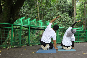 Back view of Asian muslim couple doing yoga practice on yoga mat at the greenery park. 