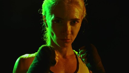 After hard training. Muscled woman, female professional boxer finishing workout in dark smoky gym in neon light. Sport, action, power, energy concept.
