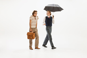 Fototapeta premium Portrait of two seriously looking man in retro style outfit walking isolated over white studio background. Diversity of emotions