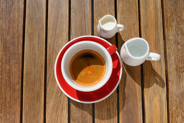 Cup of aromatic hot coffee, milk and water on wooden table, flat lay