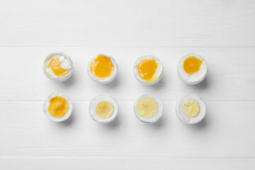 Different readiness stages of boiled chicken eggs on white wooden table, flat lay