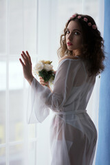 Delicate boudoir color photo of a young beautiful girl with curly hair in a bright room, shot with...