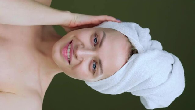 Close-up of woman with smooth healthy skin. Touching her face gently, smiling. Portrait of girl model in white bathrobe and towel posing. Skincare concept.