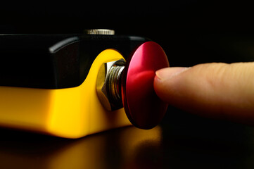 Macro photo of an emergency stop button on a remote controller for ship's crane. A finger is pushing red button. Nuclear weapon - start button. Military danger - risk of war.