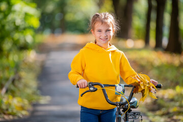 Fototapeta na wymiar Portrait of a smiling girl in yellow sweatshirt with bicycle in an autumn park.
