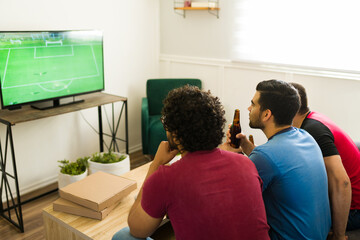 Rear view of hispanic friends watching a soccer championship in the living room