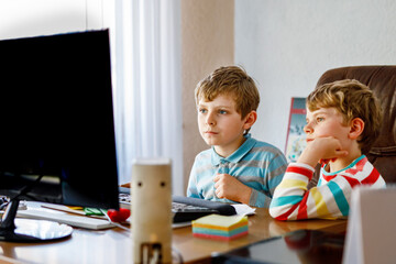 Two little kids boys playing computer games on desktop pc. Modern addict activity for children. Siblings and friends gaming at home.