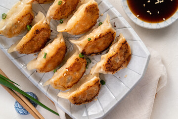 Pan-fried gyoza dumpling jiaozi in a plate with soy sauce on white table background.