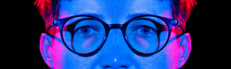 Fragment of a woman's face with an eyes and glasses on a black background in neon light.