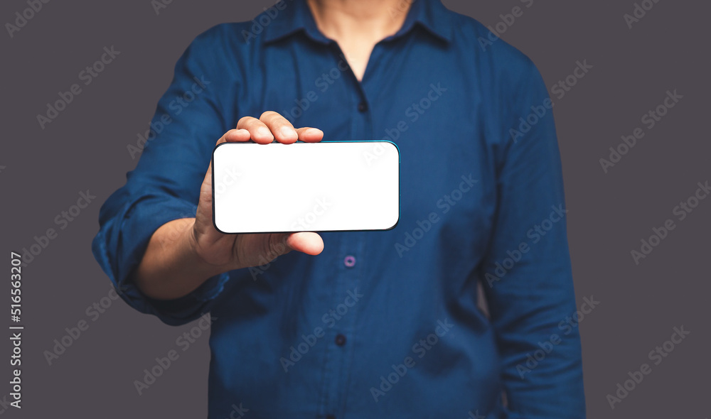 Poster close-up of hand holding a horizontal mobile phone with a blank white screen while standing on a gra