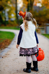 Little toddler girl dressed as a witch trick or treating on Halloween. Happy child outdoors, with...