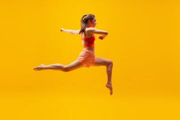 Fototapeta na wymiar Full-length portrait of young slim girl running isolated on bright yellow background. Modern sport, action, motion, summer, vacation, youth concept.