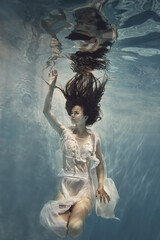A girl in a white dress with lace swims underwater as if flying