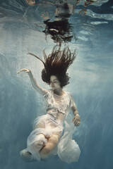 Fototapeta premium A girl in a white dress with lace swims underwater as if flying