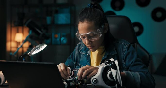 Happy young girl develops robotics skills, fixes electronics that power toy, connects cables, wires, builds her own robot for school project.