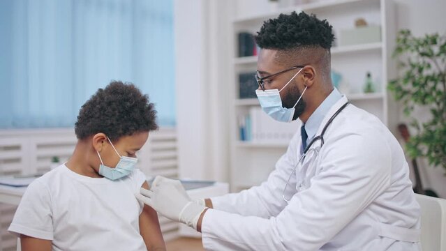 Black male doctor making vaccine injection to a child, childhood immunization