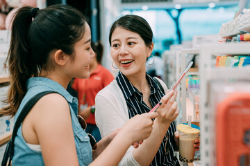 portrait happy asian girl friends are discussing the pens they choose while shopping in bright stationery store together during summer holiday.