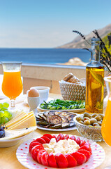 Home-made fresh summer breakfast with orange juice, cherry tomatoes, cheese, olives, cucumber, eggs a cup of coffee on the balcony with sea view.  Background concept idea.
