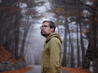 Young handsome man posing in autumn forest on road. young hipster guy with backpack , traveller standing in woods, Hiking, Forest, Journey, active healthy lifestyle, adventure, vacation concept.