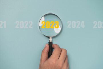 Hand holding magnifier glass with 2023 year among other year for focus new business year concept.