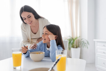 Obraz na płótnie Canvas happy babysitter looking at smiling girl having breakfast in kitchen.