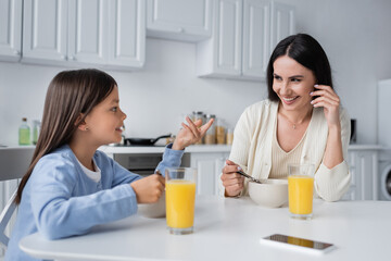 girl talking to happy nanny near bowls with breakfast and fresh orange juice.