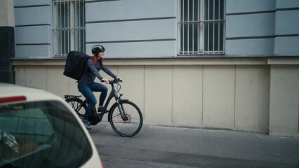 Female courier on bicycle with thermal backpack on way to deliver food to customers.