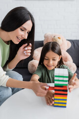 happy babysitter playing wood blocks game with girl in living room.