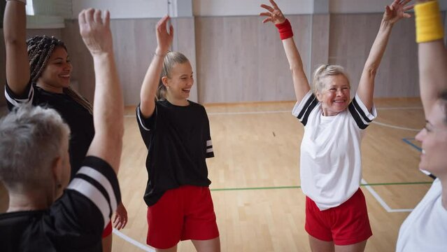 Group of young and old women in gym stacking hands together, sport team players.
