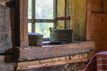 An old cast-iron coal iron made in the 19th century on the windowsill of an old wooden house. The interior of an old house. Dark log walls of the house. Rustic architecture.