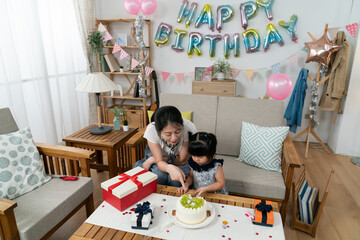 high angle shot of asian mother teaching toddler baby to use knife to cut cake with hand gesture in...