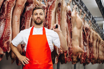 Fototapeta na wymiar Young butcher at the meat factory standing by the hanging meat
