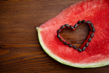 The watermelon slice is beautifully decorated with a carved heart.Bright and juicy watermelon, an appetizing piece with red pulp and dark bones.Banner with copyspace.Symbol of summer