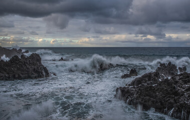 Obraz premium Rock and water lines in a black sand beach with moody cliffs on the background in Seixal at stormy day. October 2021. Madeira, Portugal